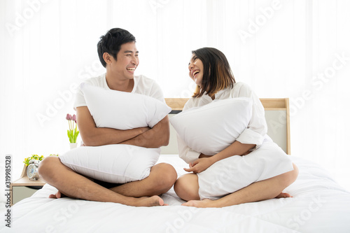 Funny and romantic Asian couple's portrait in bedroom with natural light from window, concept of relationship between husband and wife and being a family.