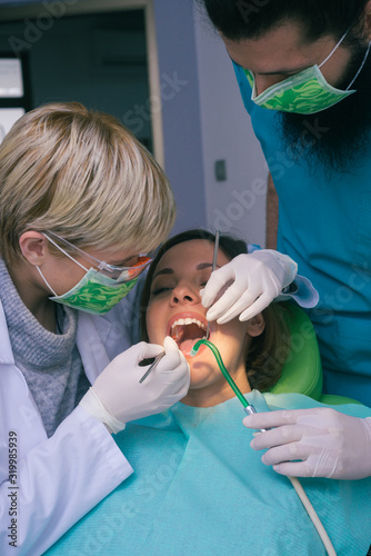 Professional male and female dentists examining woman s teeth in dental office