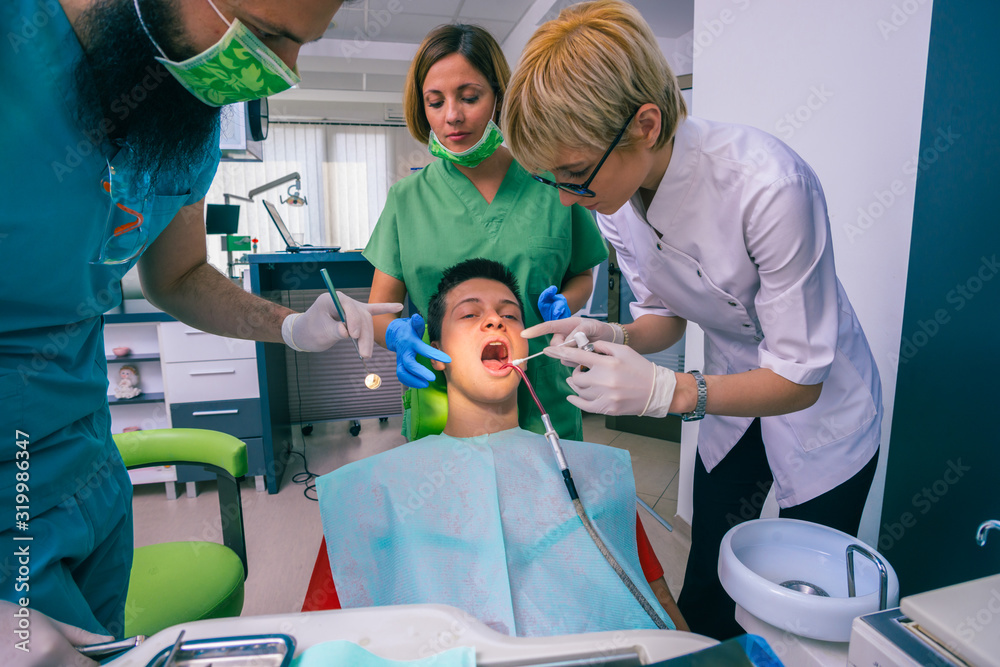 Team of dentists treating the teeth of their young boy patient using their dental tools. Team of dentists treating the teeth of their young boy patient using their dental tools.