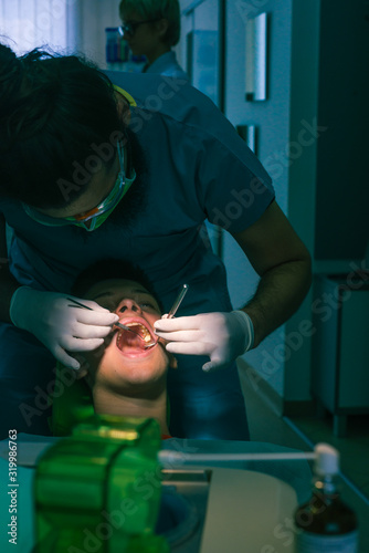 The dentist is examining teenage boy s teeth in the dentist chair in the dental office