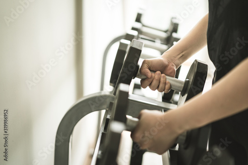 Sport woman picking up a dumbbells from dumbbell rack.