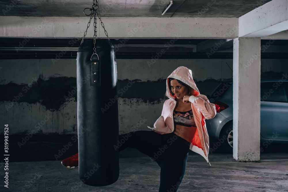 Young sportswoman doing high kick during boxing exercise in a garage.