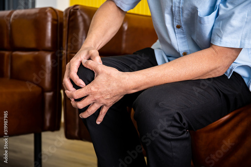 Elder man sitting on sofa because he hurting his knee. Health care in senior people concept.