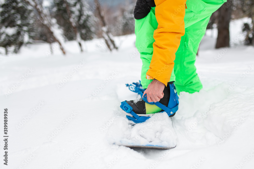 Snowboarder straps in his legs in snowboard boots close up. Snowboarder straps in his legs in snowboard boots close up.