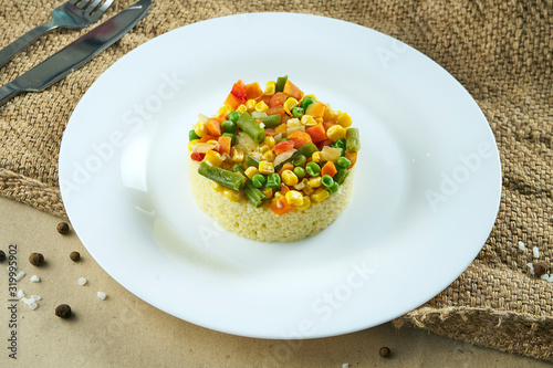 Healthy vegetarian food - porridge couscous with steamed vegetables on a white ceramic plate on rustic background. Tasty food flat lay photo