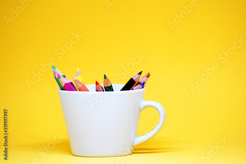 Coloured pencil or colorful Crayon for drawing on the white cup isolated with yellow pastel background Back to school concept 