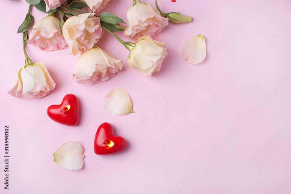 Two red heart-shaped candles and pink flowers on a pink background. View from above
