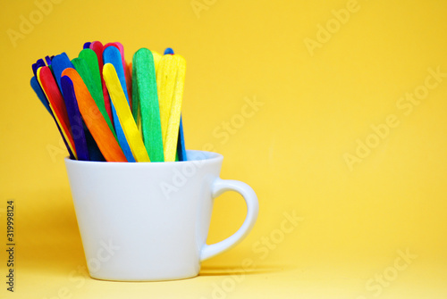 Colorful Ice cream stick on the white cup isolated with yellow pastel background -  Decorate Back to school concept with copy space