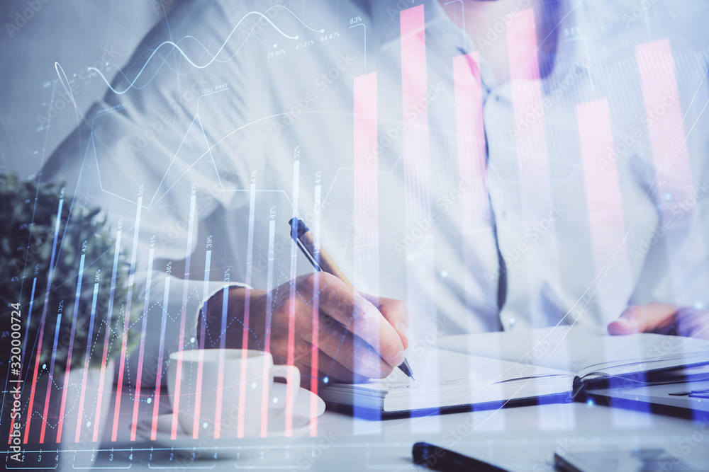 Double exposure of man's hands writing notes of stock market with forex chart.