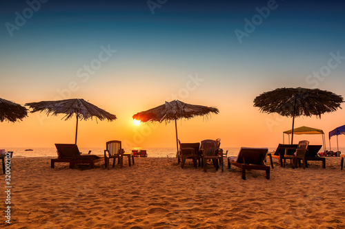 Sun umbrellas with lounge chairs at sunset on a tropical sunny beach in GOA, India