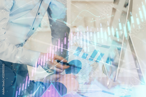 Double exposure of chart with businessman typing on computer in office on background. Concept of hard work.