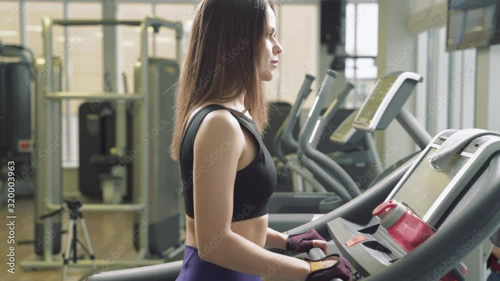 Fitness woman doing cardio training walking on treadmill in gym. Athletic girl using run machine in fitness center. Fitness woman doing cardio training walking on treadmill in gym. Athletic girl using run machine in fitness center.