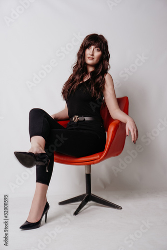 Young beautiful girl in business suit, shoes sitting on red chair, white background, business lady, young cute brunette