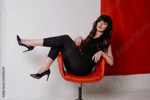 Young beautiful girl in business suit, shoes sitting on red chair, white background, business lady, young cute brunette photo