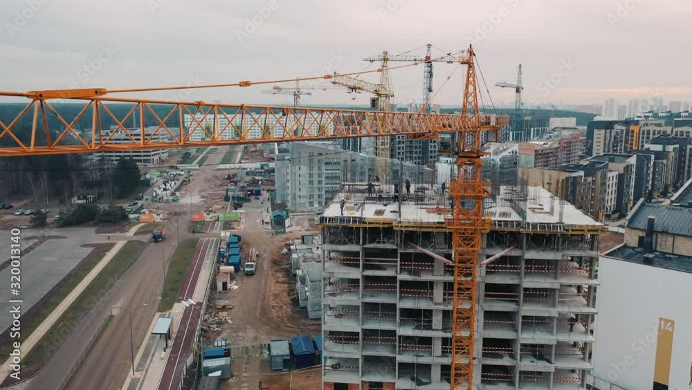 Slab-constructed apartment blocks, city-houses and town-houses building by workers. Aerial view from drone flying near crane on construction site against backdrop of modern urban area. Slab-constructed apartment blocks, city-houses and town-houses building by workers. Aerial view from drone flying near crane on construction site against backdrop of modern urban area.