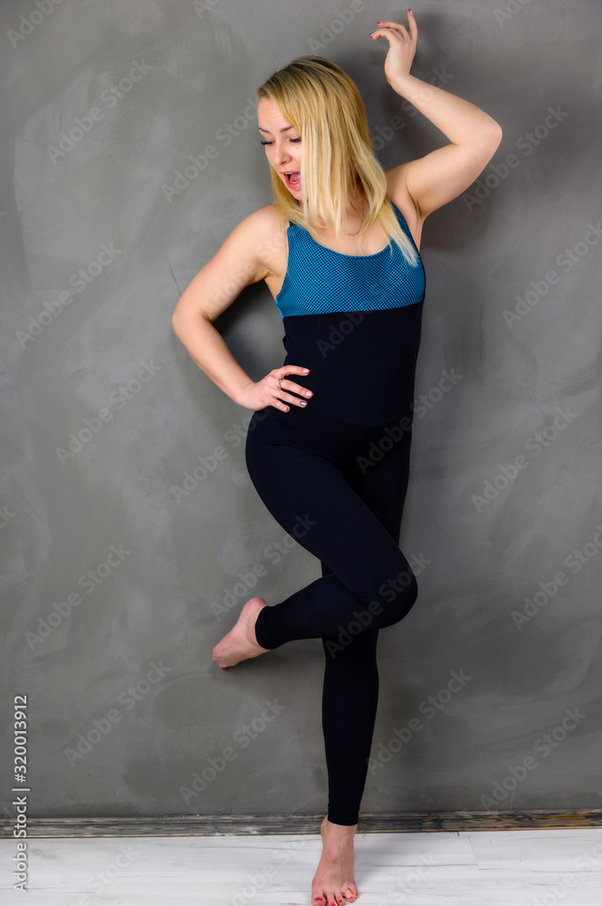 The concept of one fitness. Full-length photo of a pretty slender blonde woman athlete in a tracksuit on a gray background. Standing in different poses with emotions and a smile. The concept of one fitness. Full-length photo of a pretty slender blonde woman athlete in a tracksuit on a gray background. Standing in different poses with emotions and a smile.