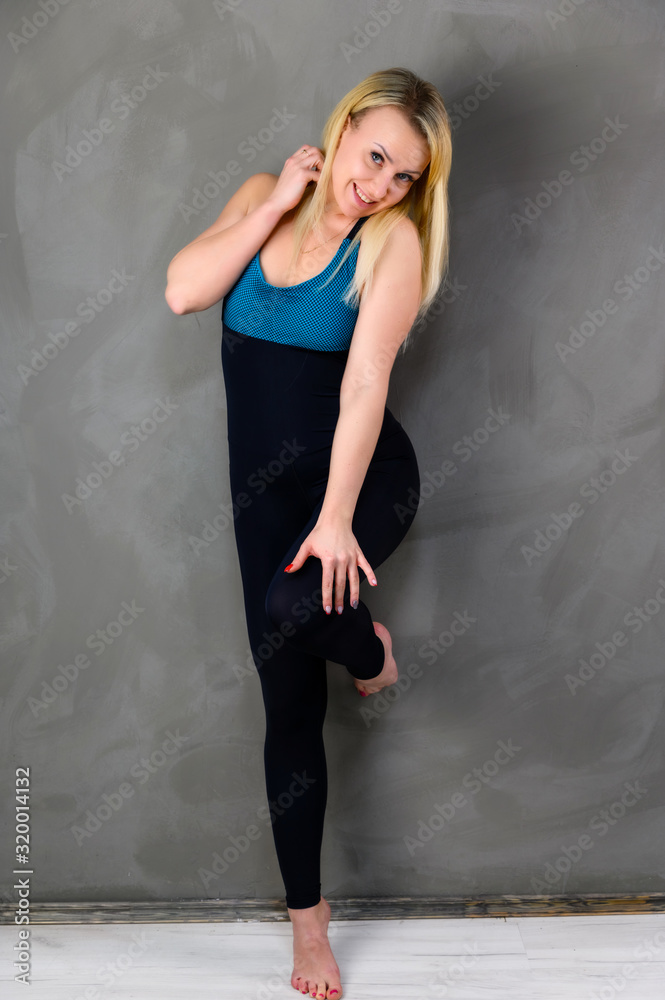The concept of one fitness. Full-length photo of a pretty slender blonde woman athlete in a tracksuit on a gray background. Standing in different poses with emotions and a smile. The concept of one fitness. Full-length photo of a pretty slender blonde woman athlete in a tracksuit on a gray background. Standing in different poses with emotions and a smile.