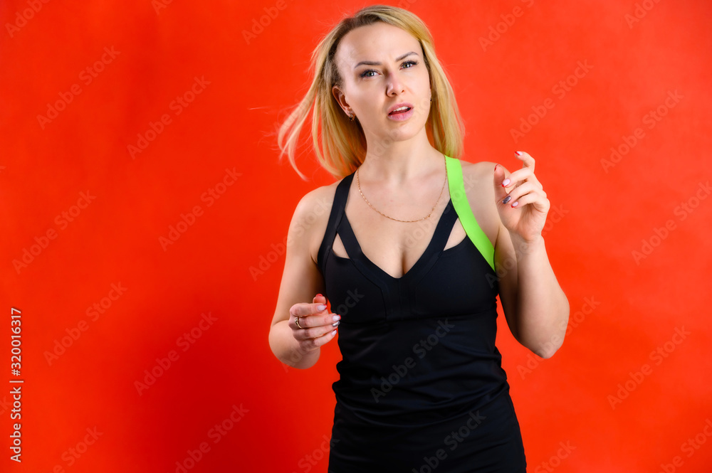 Photo of a beautiful pretty slim woman blonde sportswoman in a tracksuit on a red background. The concept of fashionable fitness. Standing in different poses with emotions and a smile. Photo of a beautiful pretty slim woman blonde sportswoman in a tracksuit on a red background. The concept of fashionable fitness. Standing in different poses with emotions and a smile.