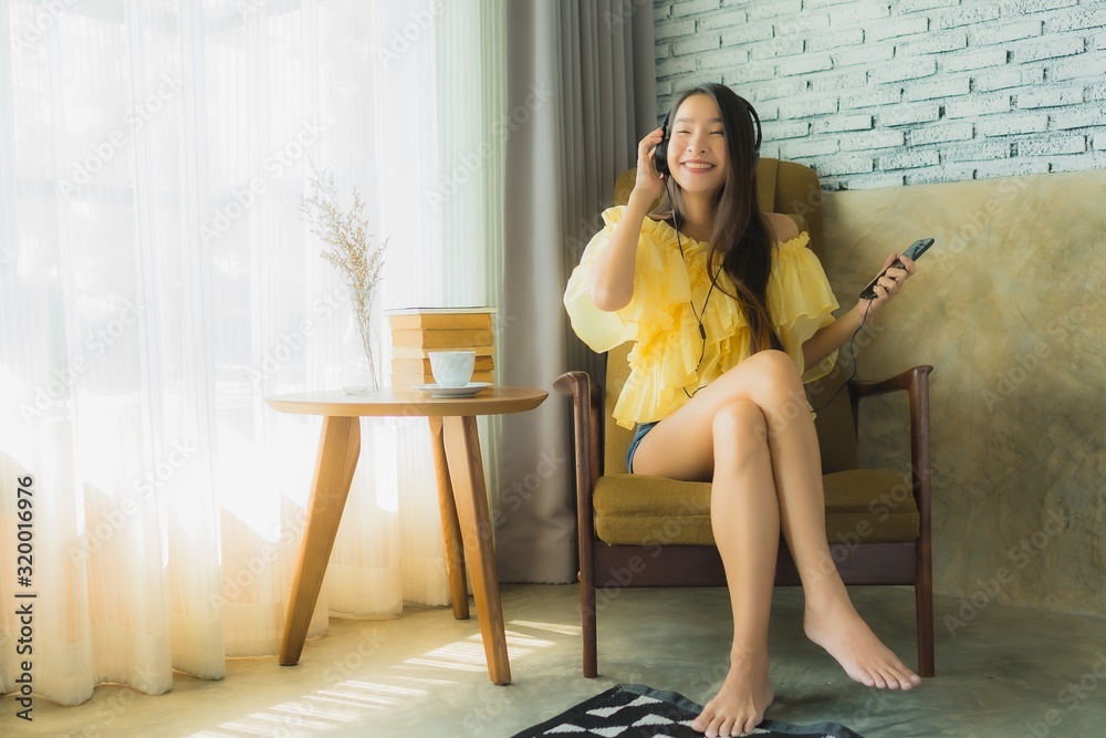 Obraz premium Portrait young asian woman sit on chair listen music with mobile phone coffee and book