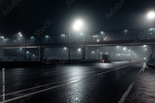 Foggy misty night road and overhead pedestrian bridge illuminated by street lights