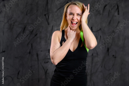 The concept of glamorous fitness. Photo of a beautiful pretty slim woman blonde sportswoman in a tracksuit on a gray background. Standing in different poses with emotions and a smile.