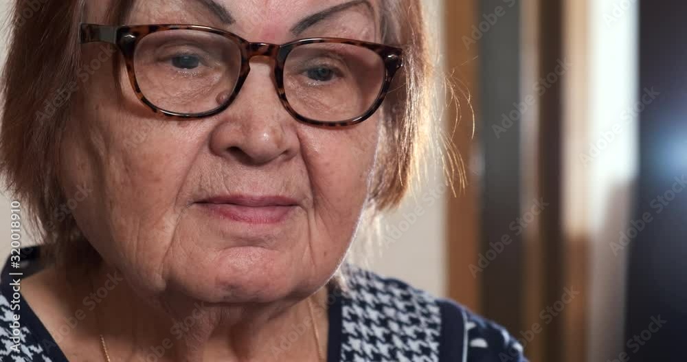 Close-up of face of elderly woman, grandmother for eighty years, looks at monitor screen, works at computer, prints text, glasses, slight smile on her face, modern pensioner, versed in technology Close-up of face of elderly woman, grandmother for eighty years, looks at monitor screen, works at computer, prints text, glasses, slight smile on her face, modern pensioner, versed in technology