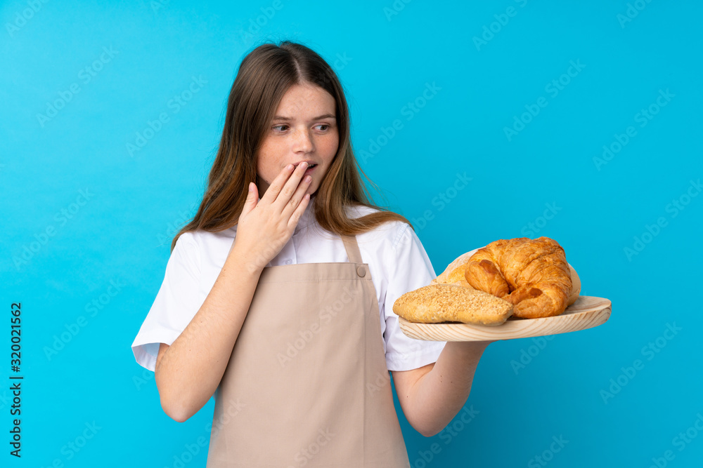 Ukrainian teenager chef uniform. Female baker holding a table with several breads with surprise and shocked facial expression Ukrainian teenager chef uniform. Female baker holding a table with several breads with surprise and shocked facial expression