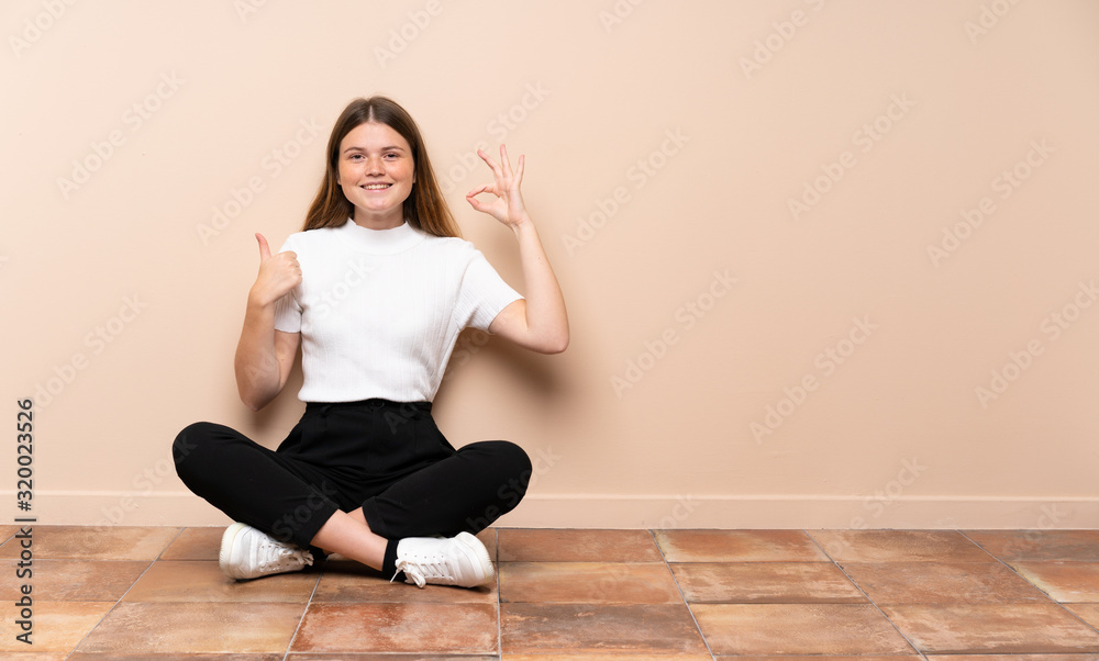 Ukrainian teenager girl sitting on the floor showing ok sign and thumb up gesture Ukrainian teenager girl sitting on the floor showing ok sign and thumb up gesture