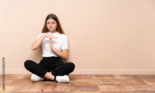 Ukrainian teenager girl sitting on the floor making time out gesture