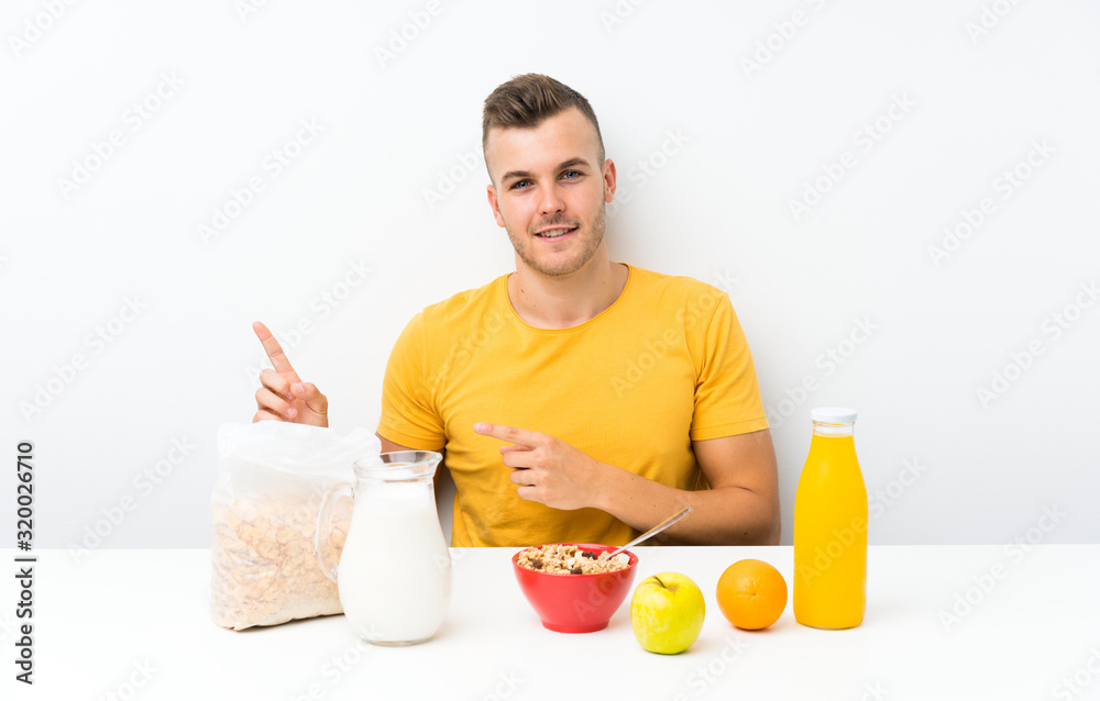Young blonde man having breakfast pointing finger to the side Young blonde man having breakfast pointing finger to the side
