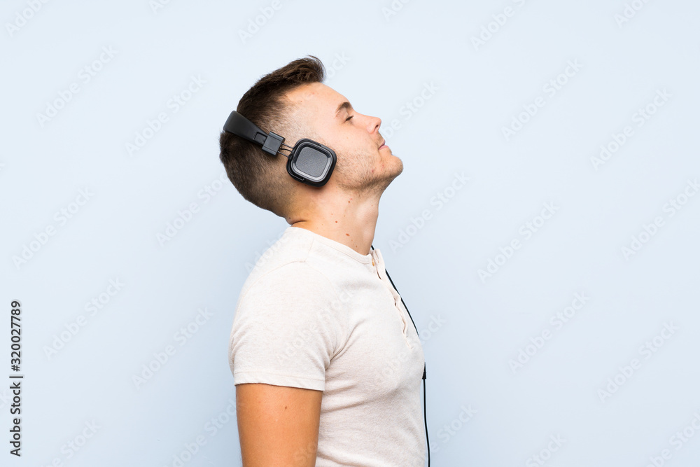 Young handsome blonde man over isolated blue background listening to music with headphones Young handsome blonde man over isolated blue background listening to music with headphones