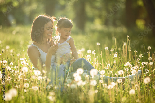 Portrait of happy mother and her little child on spring background. Cheerful family at dandelion field.Mom and her cute daughter outdoors.
