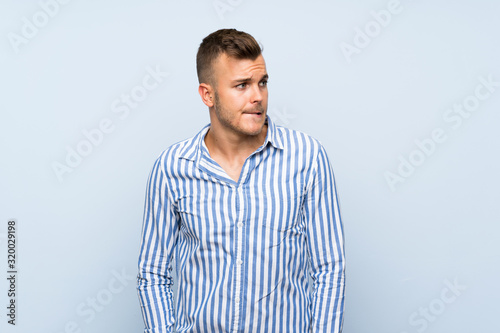 Young handsome blonde man over isolated blue background with confuse face expression