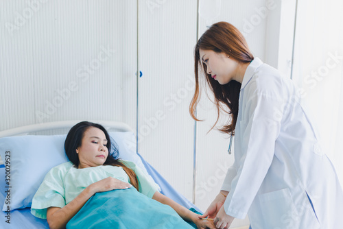 Asian woman doctor visits the patient lying in the hospital bed.