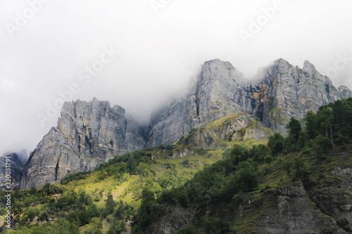 View of the sharp tops of the rocks in the clouds amd green slopes in Cirque du Fer à Cheval, Upper Savoie, beauty of French Alps