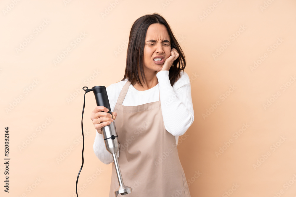 Young brunette girl using hand blender over isolated background with toothache