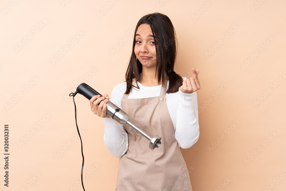 Young brunette girl using hand blender over isolated background making money gesture Young brunette girl using hand blender over isolated background making money gesture
