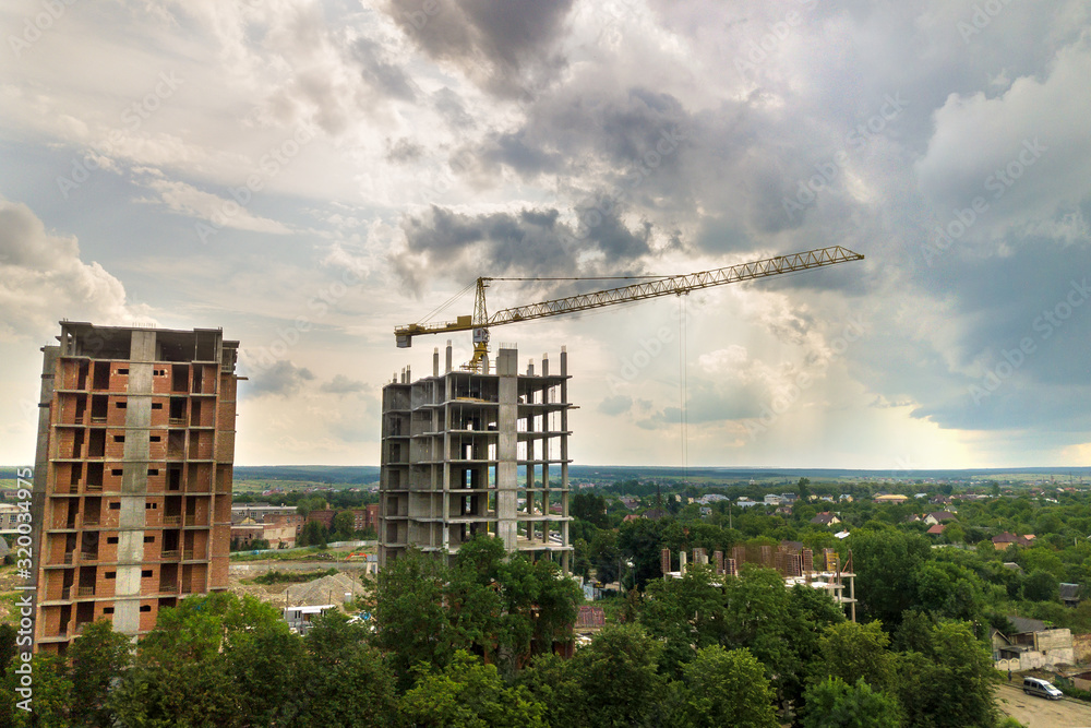 Aerial view of tower lifting crane and concrete frame of tall apartment residential buildings under construction in a city. Urban development and real estate growth concept. Aerial view of tower lifting crane and concrete frame of tall apartment residential buildings under construction in a city. Urban development and real estate growth concept.