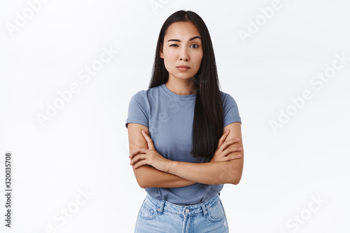 Skeptical and doubting young asian woman cross hands over chest in bossy, professional pose, stare judgemental and hesitant as measuring your ability cope with work, raise one eyebrow unsure photo