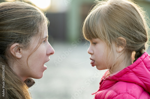 Close up portrait of young mom and her daughter girl making faces to each other outdoors.