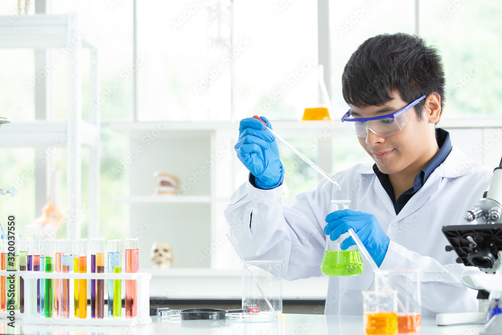 ํInvestigator checking test tubes. Man wears protective goggles. Young Research Scientist looking at Biological samples under microscope. He working in Modern Laboratory or Medical Centre. ํInvestigator checking test tubes. Man wears protective goggles. Young Research Scientist looking at Biological samples under microscope. He working in Modern Laboratory or Medical Centre.