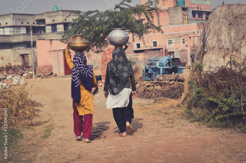 Rearview of two Women carrying water pot on their head in village area of Haryana, India