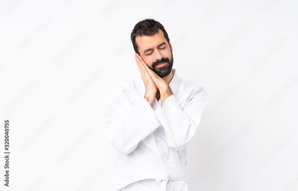 Young man doing karate over isolated white background making sleep gesture in dorable expression Young man doing karate over isolated white background making sleep gesture in dorable expression