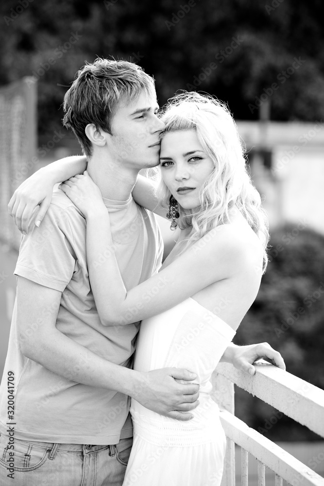 Young pretty couple charming girl in a white dress and a guy walks on the bridge on a warm summer sunny day. Concept of romantic walks Young pretty couple charming girl in a white dress and a guy walks on the bridge on a warm summer sunny day. Concept of romantic walks