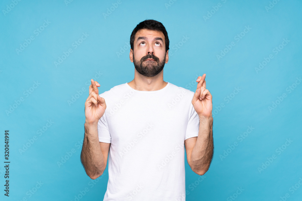 Fototapeta premium Young man with beard over isolated blue background with fingers crossing and wishing the best