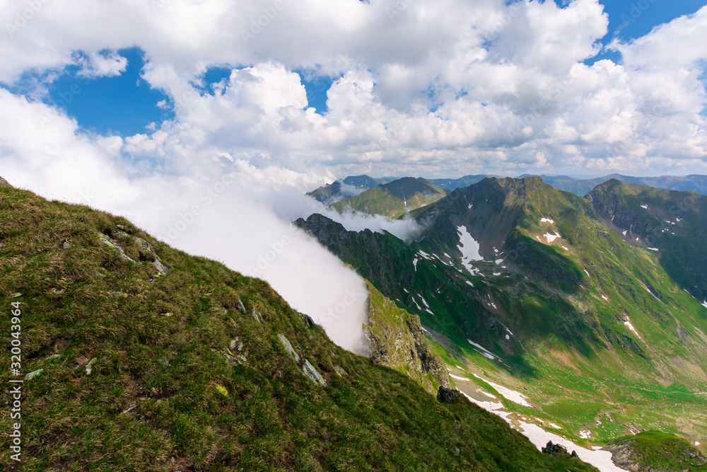 great summer scenery of high mountain range. steep slopes with rocks, grass and spots of snow. clouds on the blue sky. explore fagaras ridge of romania travel concept