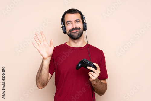 Man playing with a video game controller over isolated wall saluting with hand with happy expression