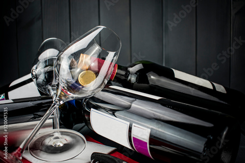 Fototapeta Naklejka Na Ścianę i Meble -  bright wine glasses lying on bottles of red wine in gray wooden space