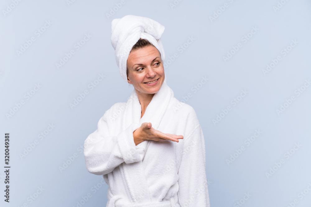 Woman in bathrobe over isolated blue background extending hands to the side for inviting to come Woman in bathrobe over isolated blue background extending hands to the side for inviting to come