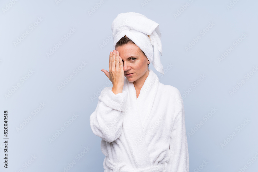 Woman in bathrobe over isolated blue background covering a eye by hand Woman in bathrobe over isolated blue background covering a eye by hand